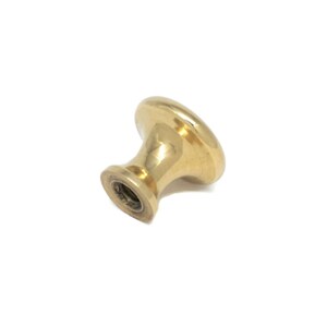 May include: A single, gold-colored cabinet knob with a rounded top and a cylindrical base. The knob is made of a shiny, metallic material and is set against a white background. This hardware is suitable for drawers and cabinets.