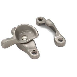 May include: A set of two silver window latches. The latch on the left has a lever handle and a small, round, recessed area. The latch on the right is a simple, curved piece with a hole in the center.
