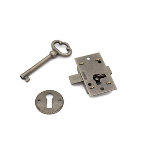 May include: Antique-style hardware set featuring a key, a keyhole cover, and a lock mechanism. The metal pieces have a tarnished, bronze finish, suggesting an aged aesthetic. The key has a decorative handle, and the lock has a visible keyhole.