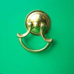May include: A gold-toned drawer pull with a rounded, decorative design. The pull is mounted on a bright green surface.