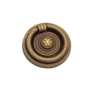 May include: A round, brass door pull with a decorative, concentric ring design. The pull has a raised, floral pattern in the center.