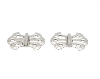 May include: Two silver-toned decorative hinges with a decorative, ornate design. The hinges are closed and ready to be installed.
