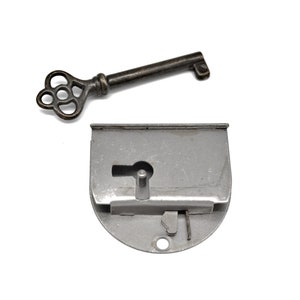 May include: A silver-colored metal lock with a keyhole and a decorative key with a floral design. The lock is attached to a metal plate.