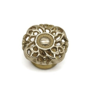 May include: A gold-toned metal cabinet knob with a decorative, intricate, floral design.
