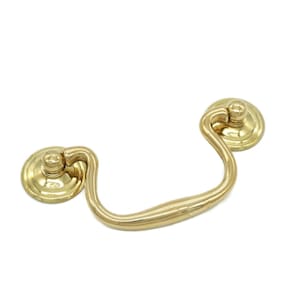 May include: A gold-toned metal drawer pull with a rounded, curved handle and two decorative knobs.