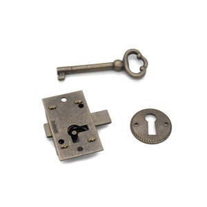 May include: An antique-style lock set with a key, lock plate, and keyhole cover. The metal pieces have a bronze finish. The key has a decorative handle. The lock plate has a rectangular shape with screw holes.