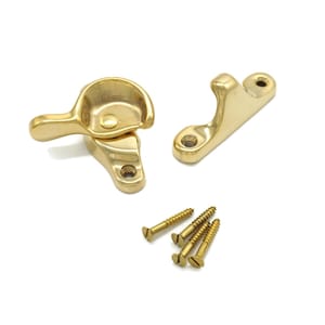 May include: A set of brass-colored window sash hardware, including a latch, a catch, and four screws. The latch has a curved handle and a rounded base. The catch is a simple, angled piece with a hole for a screw.