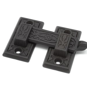 May include: Black metal door latch with an ornate design. The latch has a decorative floral pattern and a lever handle.