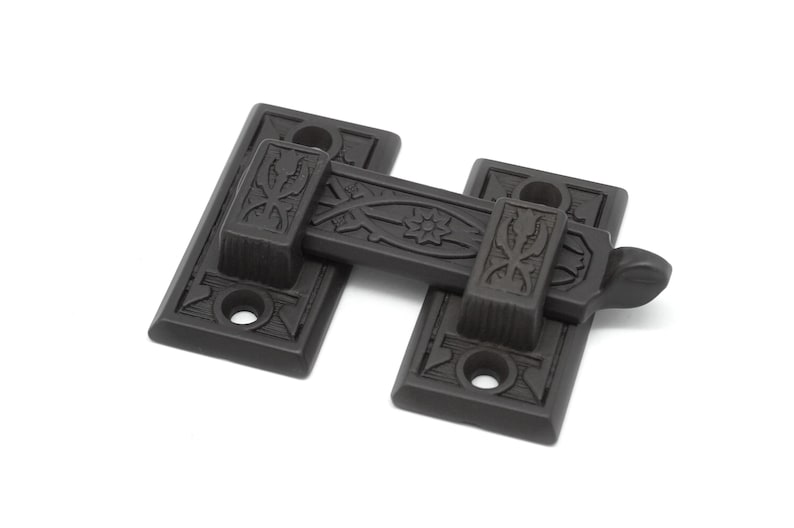 May include: Black metal door latch with an ornate design. The latch has a decorative floral pattern and a lever handle.