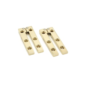 May include: Two gold-colored, rectangular hinges with multiple circular holes for screws. Each hinge is composed of two connected sections, designed to allow movement. The hinges are presented against a white background.