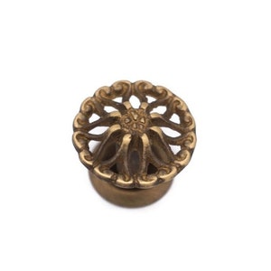 May include: A decorative brass knob with a floral design. The knob features an openwork pattern with a central flower-like element and a circular base. The brass has a warm, antique finish, and the knob is set against a white background.