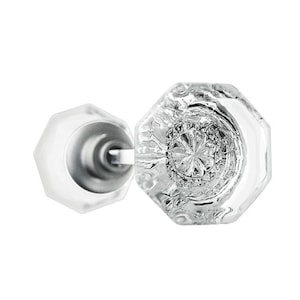 May include: Clear glass octagonal door knob with a decorative center and a silver metal base. The knob is designed with a classic, vintage aesthetic. The door knob is a home decor item.