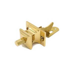 May include: A gold-toned metal door latch with a square-shaped handle and a lever mechanism. The latch is designed to be mounted on a door.