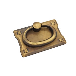 May include: Antique brass cabinet pull with a rectangular base and a ring handle. The pull has a distressed finish and decorative accents.