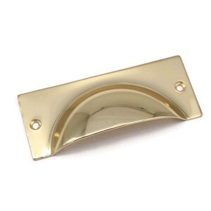 May include: A gold-toned cabinet pull with a curved, rectangular shape. The pull has a smooth, polished finish and two small holes for mounting.