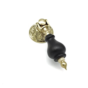 Puede incluir: Un pomo de armario de madera negra con una base de metal dorado y un diseño floral decorativo.