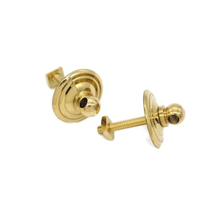 May include: Two gold metal curtain tiebacks with a round knob and a decorative plate. The tiebacks are attached to a screw.