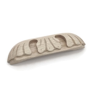 May include: A light wood cabinet pull with a carved design. The pull is shaped like a half-circle with a series of rounded, carved shapes along the top.