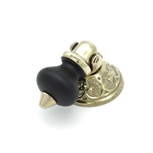 May include: A black and gold doorstop with a decorative base and a round knob. The knob is black and has a pointed tip.