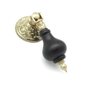 May include: A black wooden knob with a gold metal base and decorative floral design. The knob has a pointed tip and a rounded shape.
