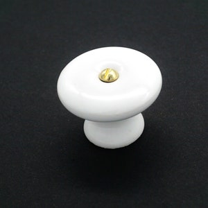 May include: White ceramic cabinet knob with a gold screw in the center.