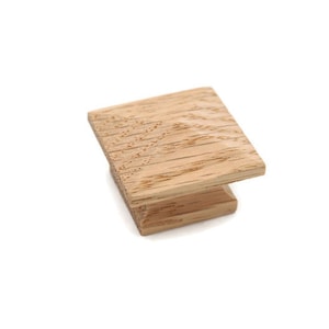 May include: A wooden cabinet knob with a square shape and a natural wood finish.