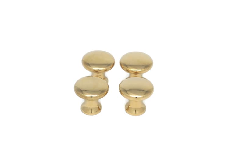 May include: Four gold-colored cabinet knobs with a smooth, rounded design. Each knob has a circular top and a cylindrical base, all in a shiny, metallic finish. The knobs are arranged in two pairs, suitable for furniture hardware.