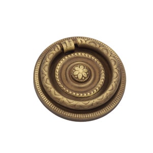 May include: A round, brass door pull with a decorative ring and a floral design in the center.