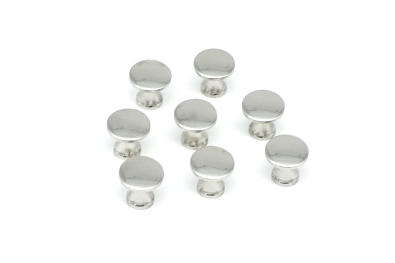 May include: A collection of eight shiny, silver-colored cabinet knobs. Each knob has a rounded, flat top and a short, cylindrical base. The knobs are arranged on a white background.