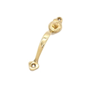 May include: A gold-toned metal door handle with a curved arm and a round knob. The handle has a small hole on the end of the arm and a small hole on the knob.