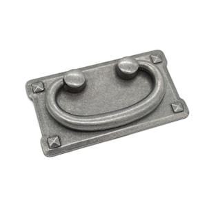 May include: A silver-toned metal drawer pull with a rectangular base and a rounded, D-shaped handle. The pull has a distressed finish and decorative accents on the corners.