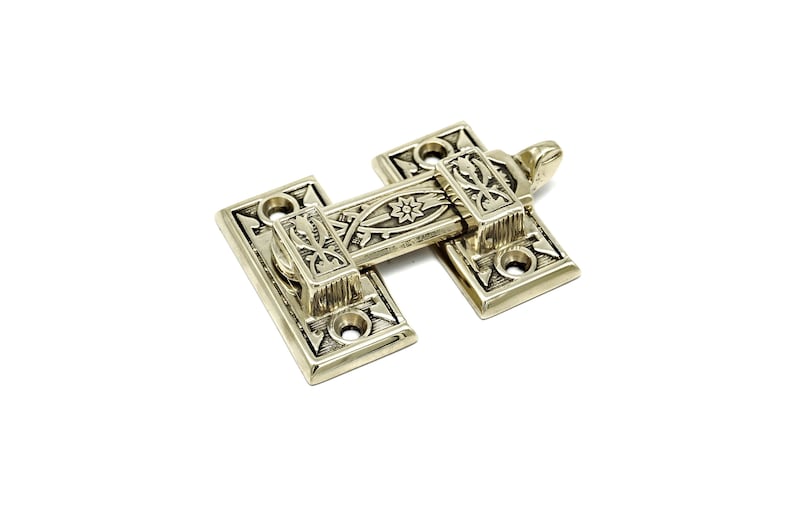 May include: A decorative brass latch with intricate floral and starburst patterns. The latch is rectangular with a central sliding bar and is designed for a door or cabinet. The metal has a polished finish, and the design is vintage-inspired.
