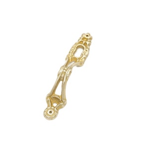 May include: A gold-toned metal decorative accent with a floral design. The accent has a keyhole shape in the center.
