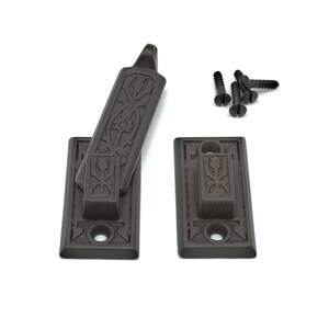 May include: A set of two black metal window latch plates with ornate designs. The latch is in the open position and includes four black screws.