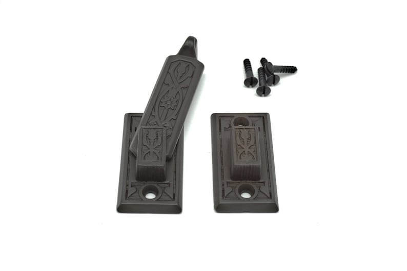 May include: A set of two black metal window latch plates with ornate designs. The latch is in the open position and includes four black screws.
