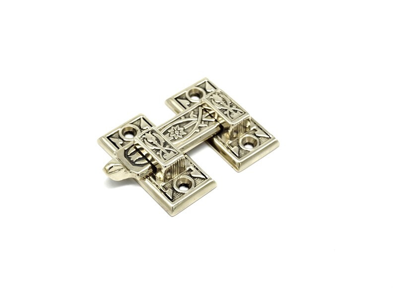 May include: A decorative, antique-style brass hinge with intricate floral and geometric patterns. The hinge is composed of two rectangular plates connected by a central bar, with a lever for opening and closing. The hardware is set against a white background.
