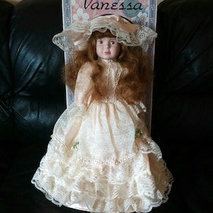 Peut inclure: Une poupée en porcelaine aux longs cheveux bruns portant une robe en dentelle blanche et un chapeau en dentelle blanche. La poupée fait partie de la collection Vanessa Doll.