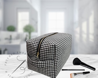 May include: A black and white gingham patterned cosmetic bag with a gold zipper. The bag is rectangular and sits on a marble surface. Makeup brushes are arranged next to the bag. The text "PATCHED EMBROIDERY & SEWING STUDIO" is in the background.