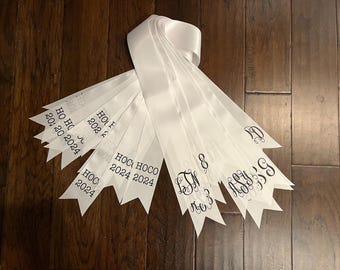 May include: White satin ribbons with black text. The text on the ribbons reads "HOC 2024", "HOCO 2024", "HO 2024", and "20 + 20 2024".