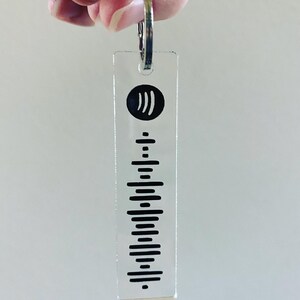 May include: A clear acrylic keychain with a black Spotify logo and a black and white barcode design.