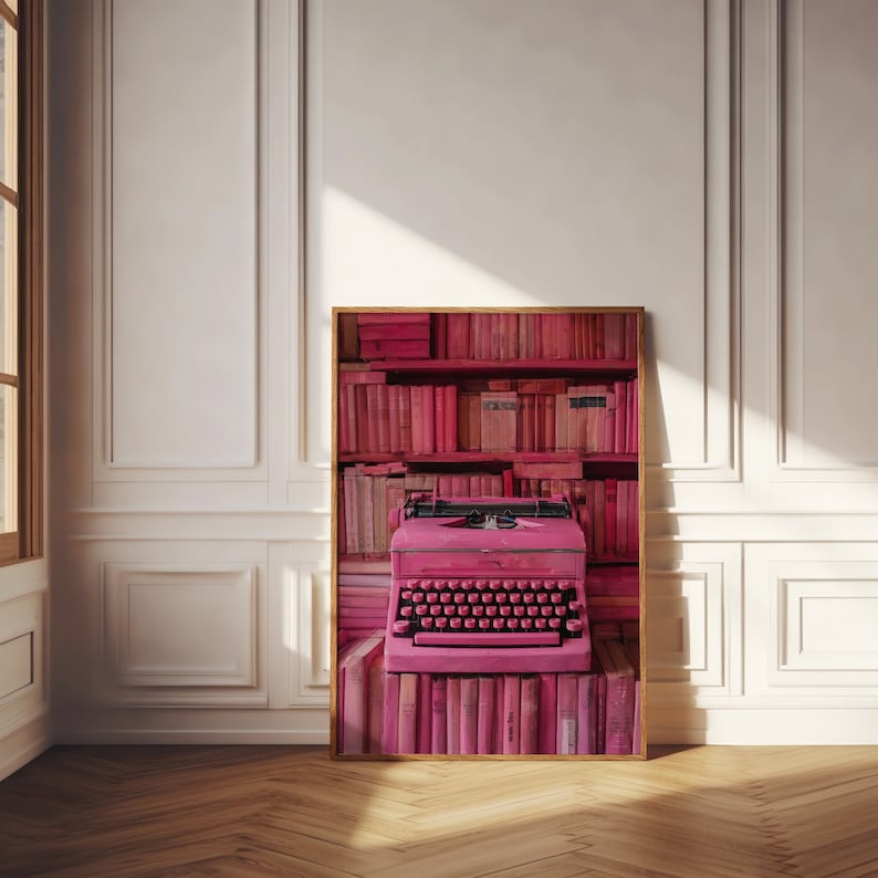 K&ouml;nnte beinhalten: Eine rosafarbene Schreibmaschine steht auf einem Regal voller rosa B&uuml;cher. Die Schreibmaschine hat ein rosa Band und einen rosa Wagenr&uuml;cklaufhebel.