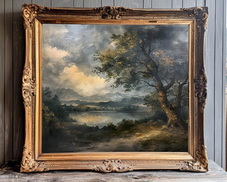 May include: A framed oil painting depicting a landscape scene with a large tree in the foreground, a lake in the middle ground, and rolling hills in the background. The sky is cloudy and the colours are muted.