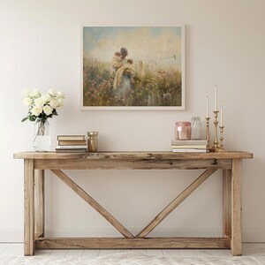 May include: A rustic wooden console table with a distressed finish and a triangular support structure. The table is decorated with a framed painting of a woman holding a child in a field of flowers, a vase of white roses, and candlesticks with gold candles.