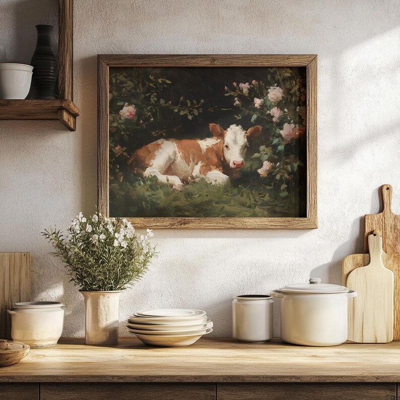 May include: A framed vintage painting of a brown and white calf resting in a grassy area surrounded by pink roses. The artwork has a rustic wooden frame and is displayed on a white wall. The scene evokes a pastoral, countryside theme.