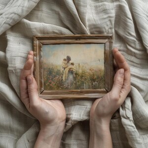 May include: A framed painting depicting a woman carrying two children in a field of wildflowers. The painting has a soft, muted color palette with shades of blue, green, and yellow.