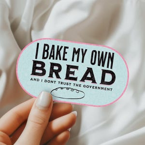 May include: A light blue and pink oval sticker with the text "I bake my own bread and I don't trust the government". A small illustration of a loaf of bread is below the text.