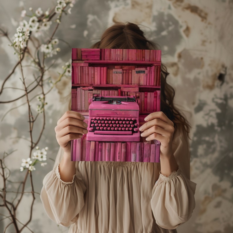 K&ouml;nnte beinhalten: Eine Frau h&auml;lt eine rosafarbene Schreibmaschine vor ihrem Gesicht. Die Schreibmaschine ist von einem B&uuml;cherregal umgeben, das mit rosafarbenen B&uuml;chern gef&uuml;llt ist.
