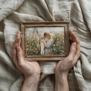 May include: A framed painting of a woman holding a baby in a garden setting. The woman is wearing a blue dress and the baby is wrapped in a white blanket. The painting is surrounded by a wooden frame.
