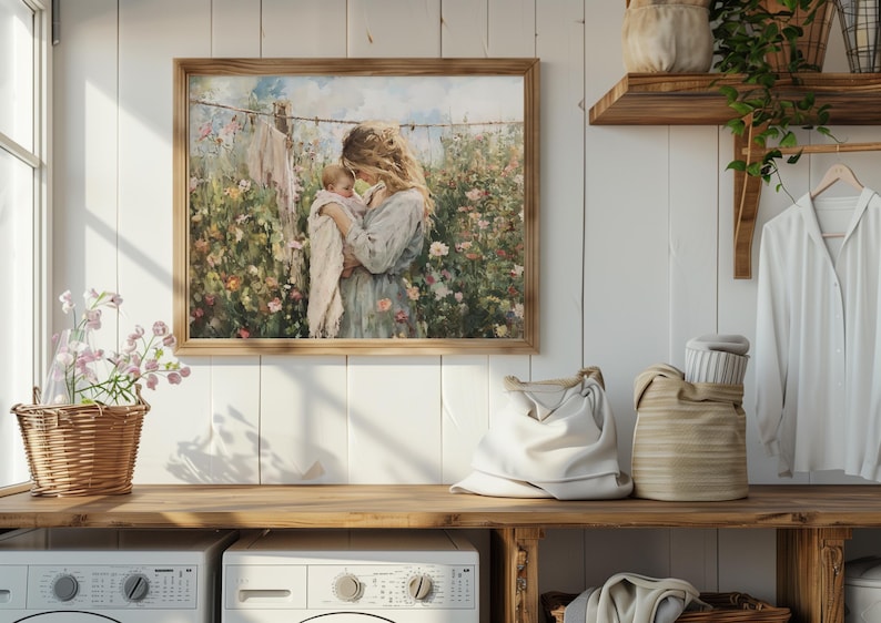 May include: A framed painting of a woman holding a baby in a field of flowers. The woman is wearing a blue dress and the baby is wearing a pink dress. The painting is set against a white wall with a wooden shelf above it.