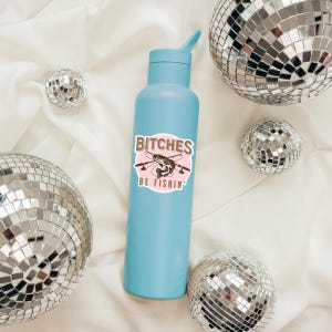 May include: A light blue water bottle with a pink and brown sticker that says "Bitches Be Fishin'" and features a cartoon fish with fishing rods. The sticker is on a light blue water bottle.